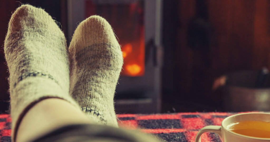 pies con calcetines abrigados y un te de frente a una chimenea 