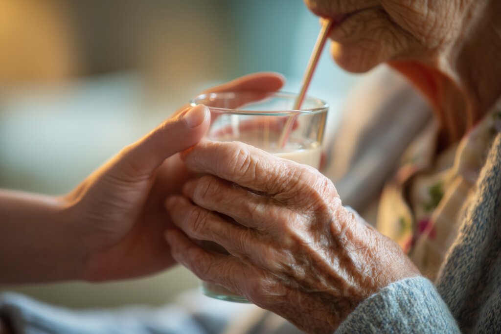 Cuidadora persona mayor persona mayor siendo ayudada a beber con una pajita de un vaso