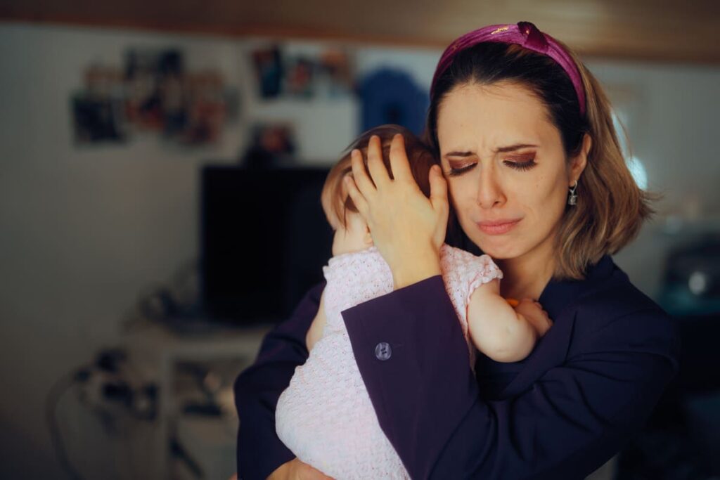 síndrome del cuidador culpable mujer sosteniendo a bebe con expresión triste como de llanto y culpa