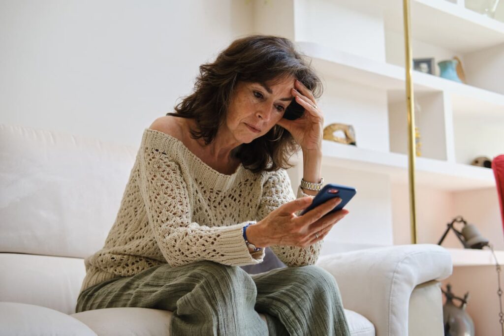 Domótica en ancianos Mujer con gesto de preocupación o seriedad mirando el móvil sentada en el sofá
