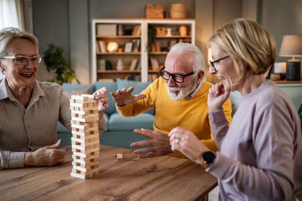 Juegos de mesa para personas mayores tres personas mayores disfrutando de jugar al juego de torre de madera en la mesa del salón