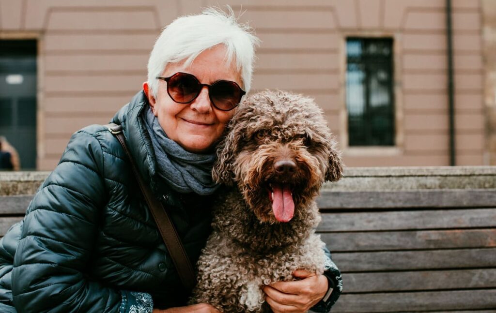 Edad para tener Alzheimer Mujer adulta con su perro en un banco de madera de la calle.