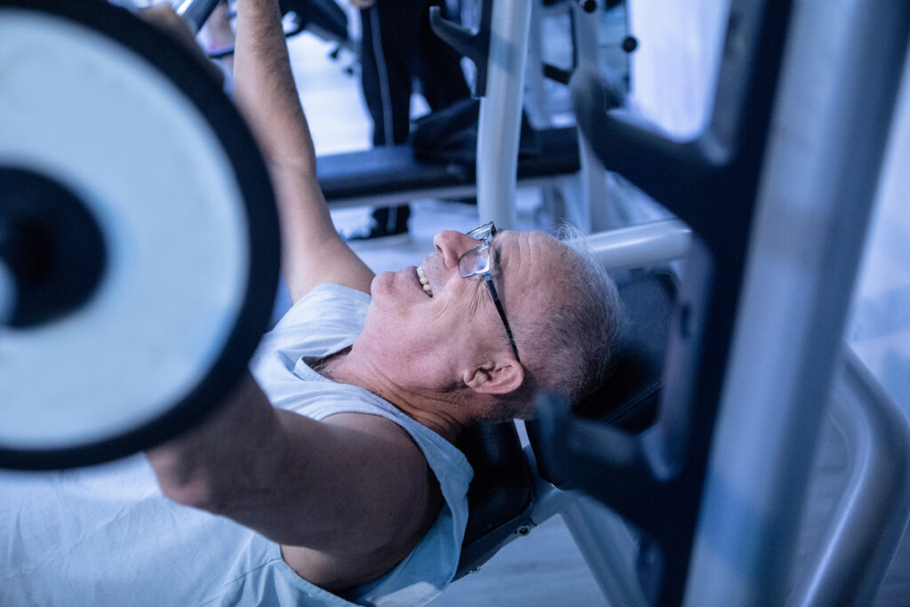 Ejercicios de fuerza para personas mayores Hombre mayor realizando ejercicios de levantar pesas en el gimnasio
