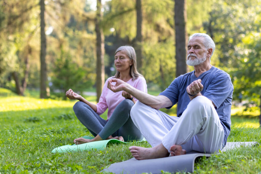 Deporte en personas mayores Dos personas mayores realizando meditación y yoga en una esterilla en el parque